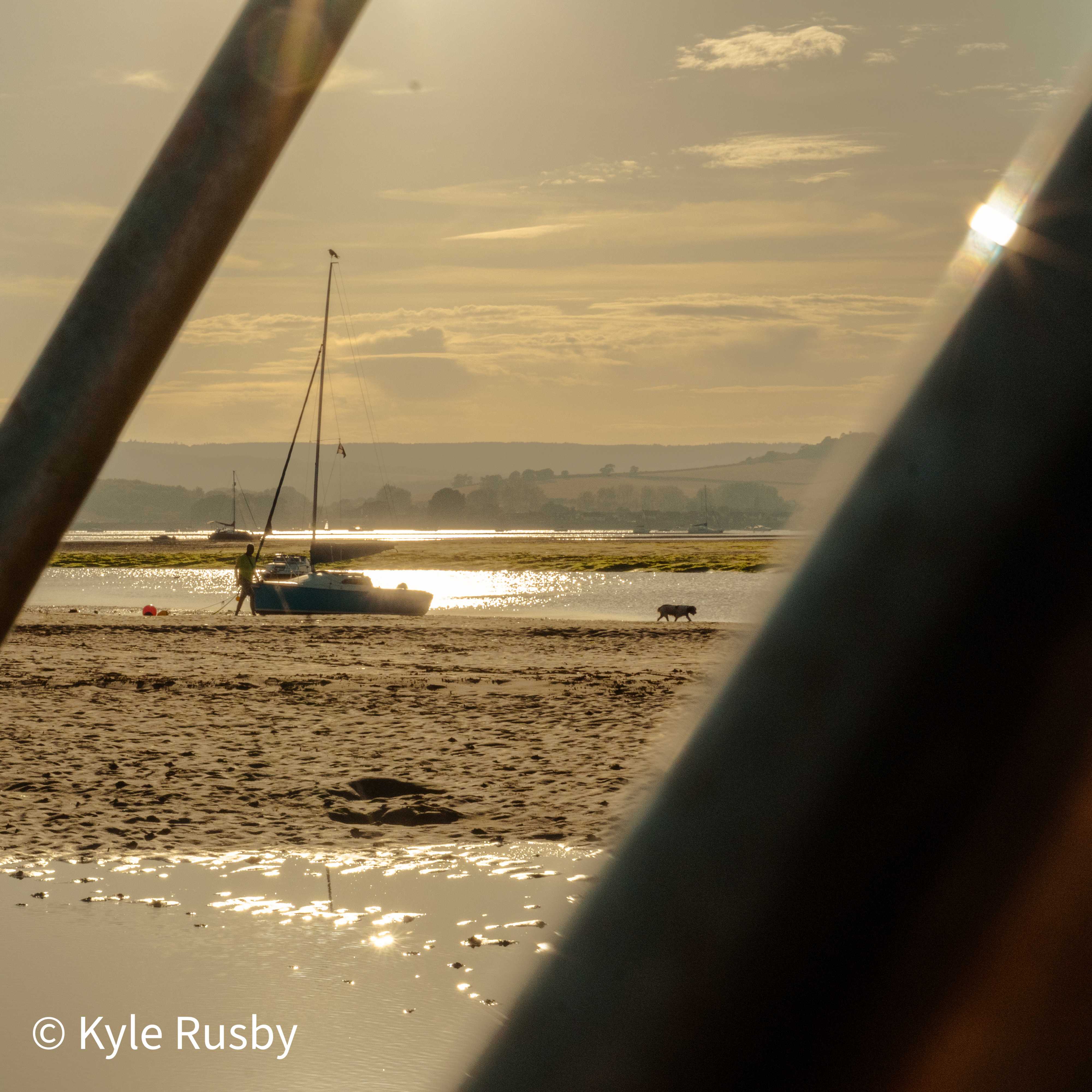 The same sailboat between railings a moment later, its skipper at the hull and the dog trotting the sand ahead